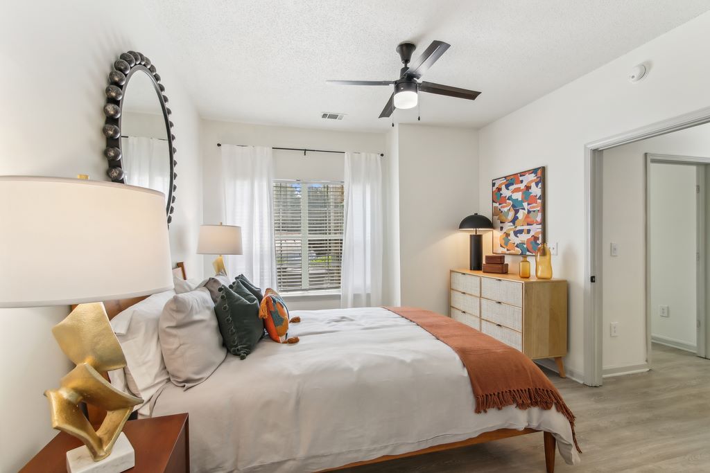 Virtually staged bedroom with a bed, dresser, nightstand, hardwood-style flooring, ceiling fan and a window.